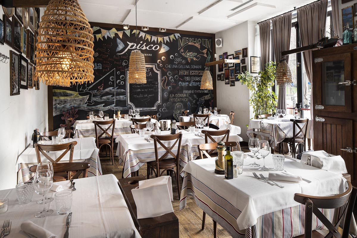 Sala ristorante Pisco con tavoli apparecchiati e parete decorata infondo
